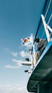 pexels-photo-28505125-28505125 A person spotted on a ship deck with the South Korean flag waving against a bright blue sky.